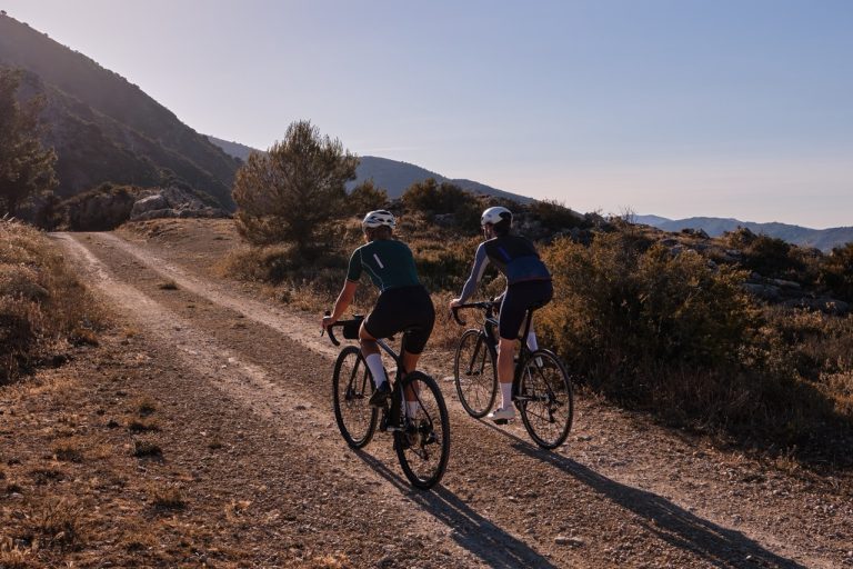 Gravel adventure..Back view of professional gravel cyclists riding uphill with mountain view at sunset. Alicante region in Spain